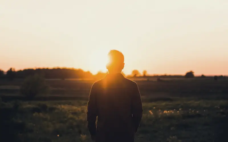 Silhouet van iemand in een veld bij zonsondergang
